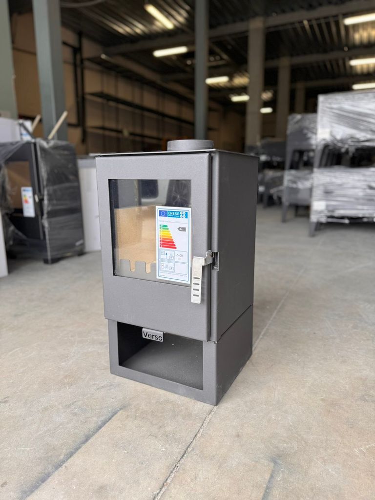 A modern wood-burning stove is displayed in a warehouse or showroom setting.