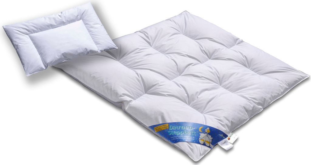 A white down comforter and a small white pillow are laid out on a white surface.