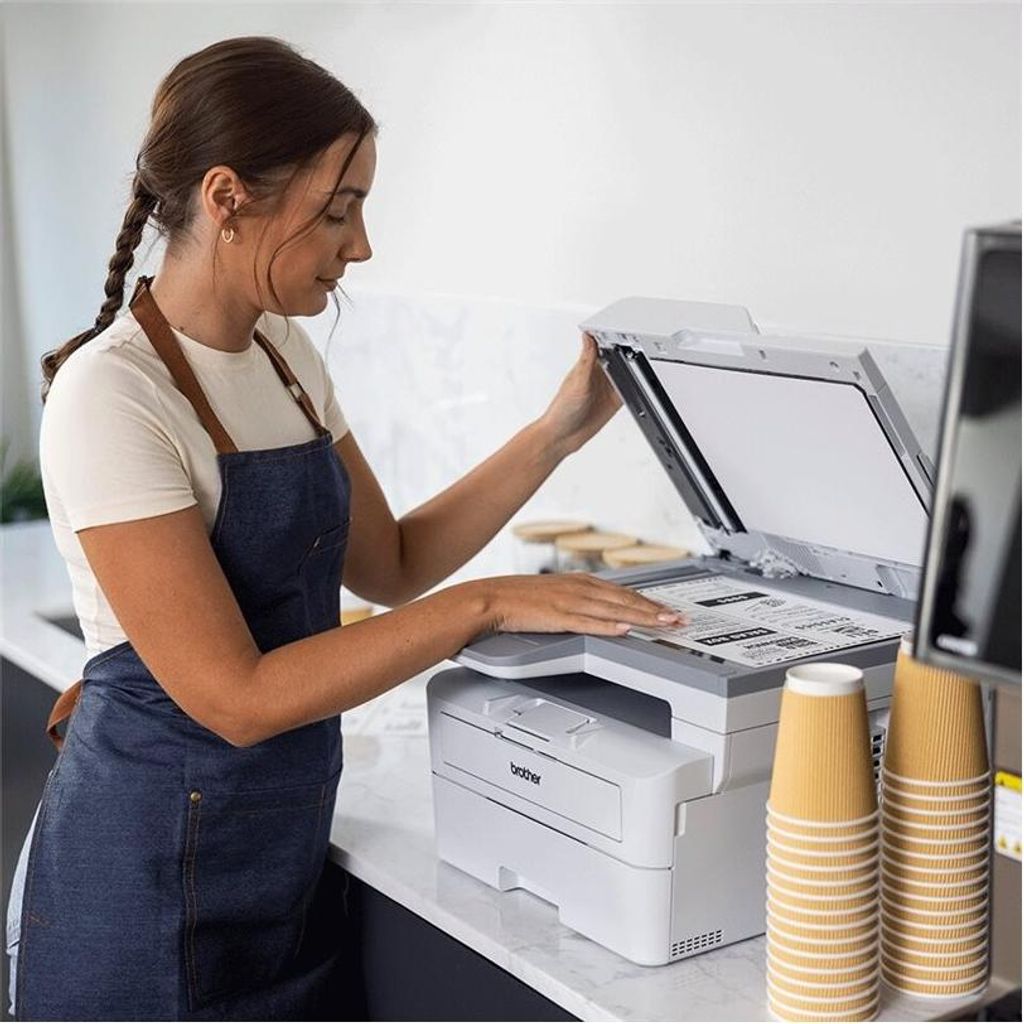 A woman is using a Brother printer in what appears to be a cafe or office setting.