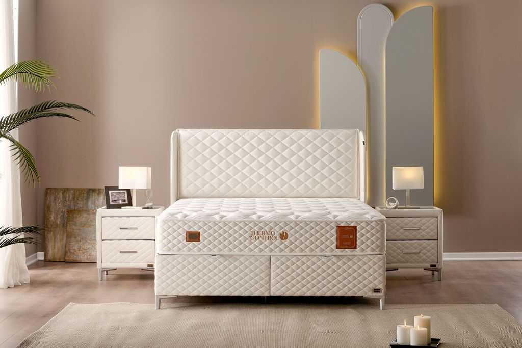 A bedroom scene featuring a white boxspring bed set with matching nightstands and lamps.