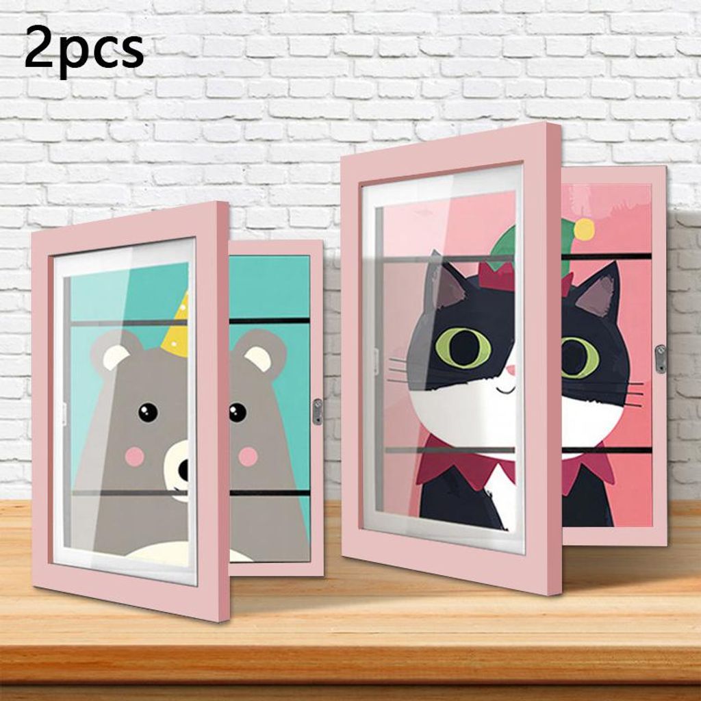 Two pink picture frames with cartoon animal drawings inside, displayed on a wooden surface against a white brick wall.
