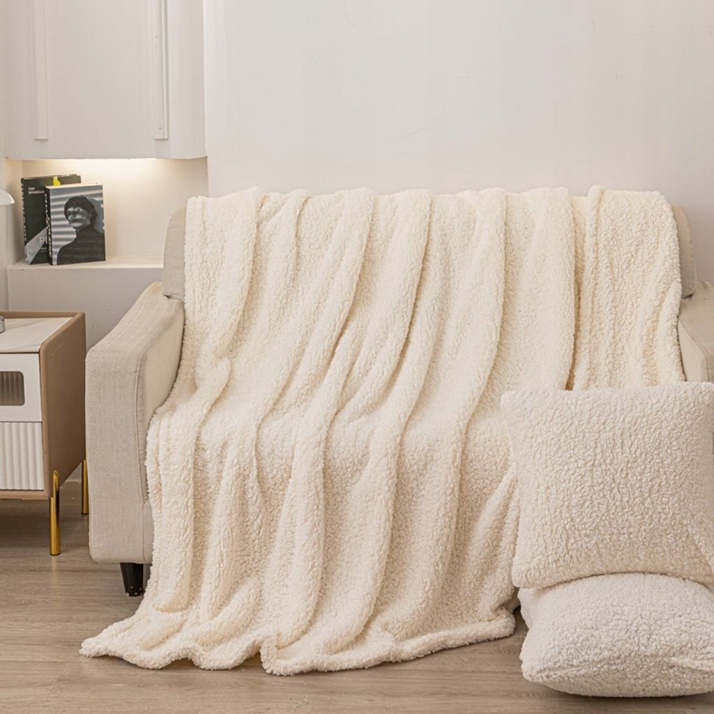 A cream-colored sherpa blanket is draped over a sofa, with two matching pillows placed in the foreground.