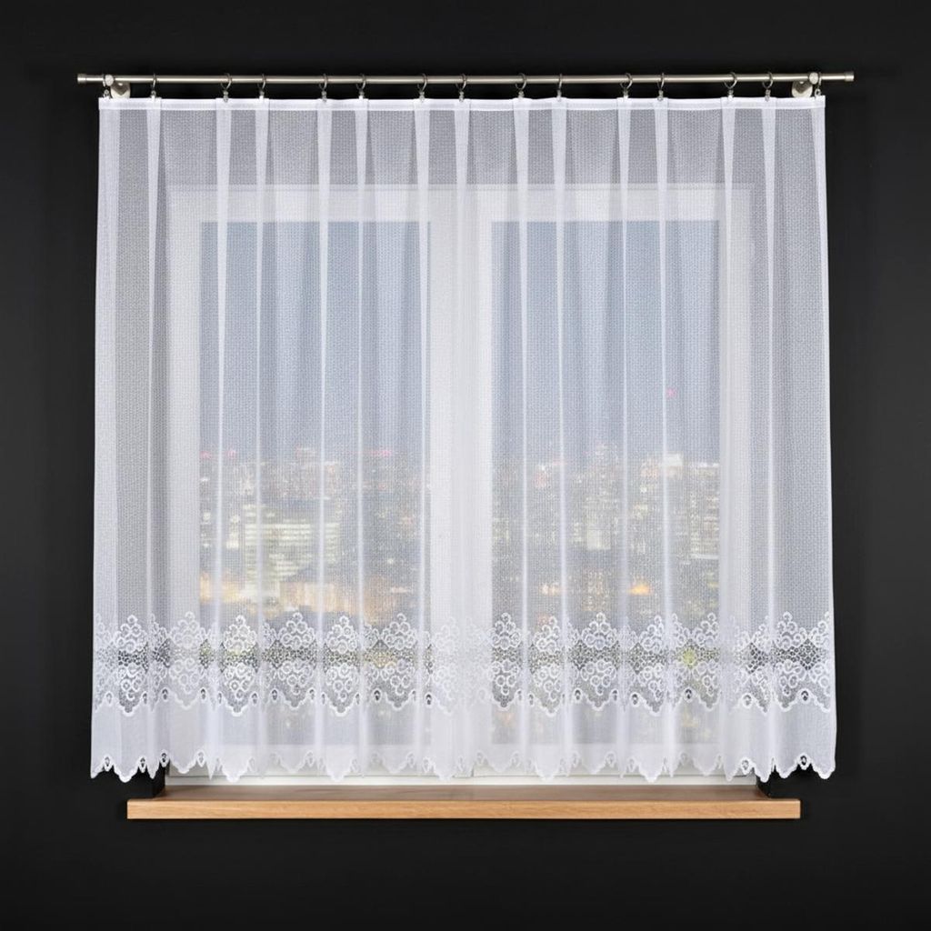A white lace curtain is hung on a window with a city view at night visible through it.