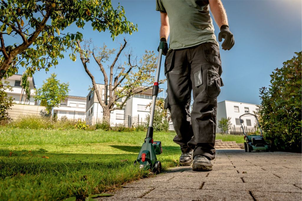 A person is using a grass trimmer in a garden with houses in the background.