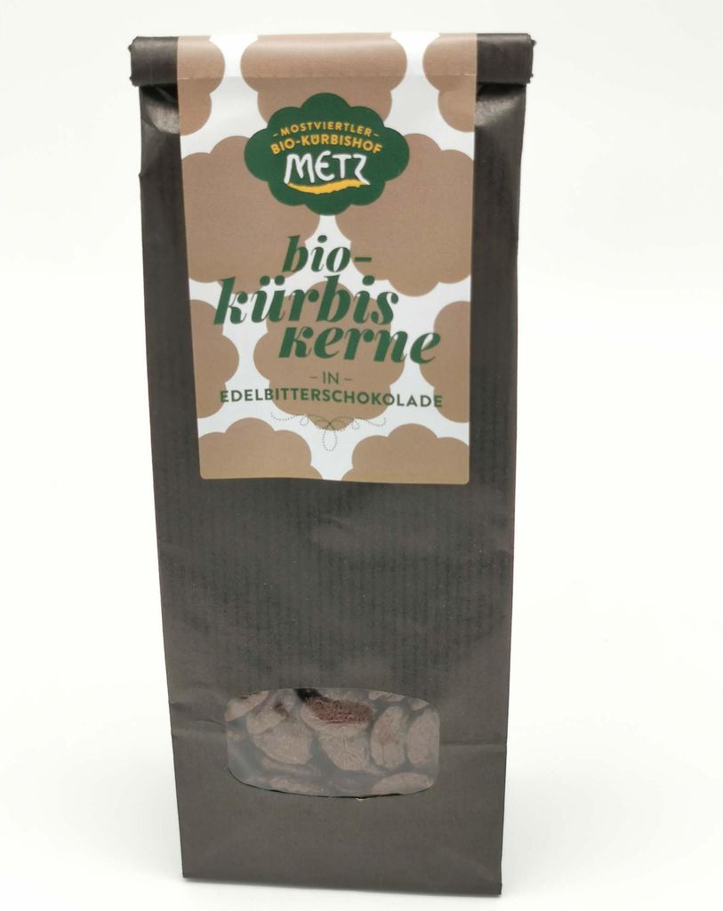 A dark brown paper bag with a label on the front, containing pumpkin seeds coated in dark chocolate.