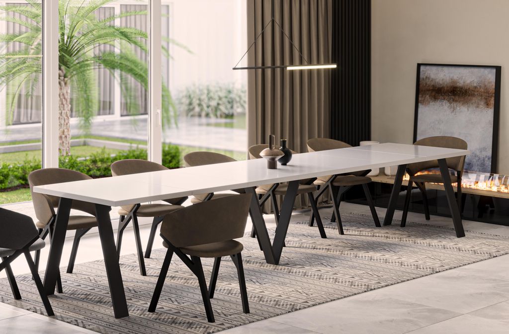 A modern dining room with a long white table and chairs, set in front of large windows overlooking a garden.