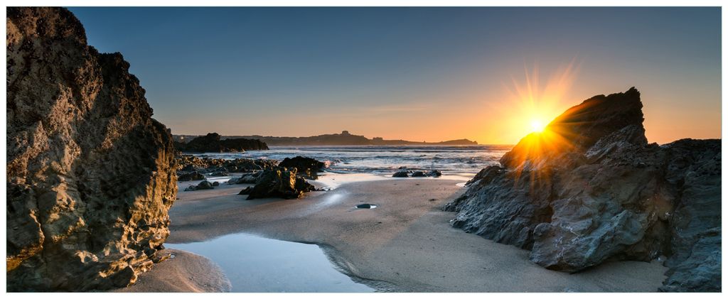 Wallario Premium Glasbild, freischwebende Optik, kräftige Farben, Größe 80 x 32 cm Motiv Sonnenuntergang hinter einem Felsen am Strand