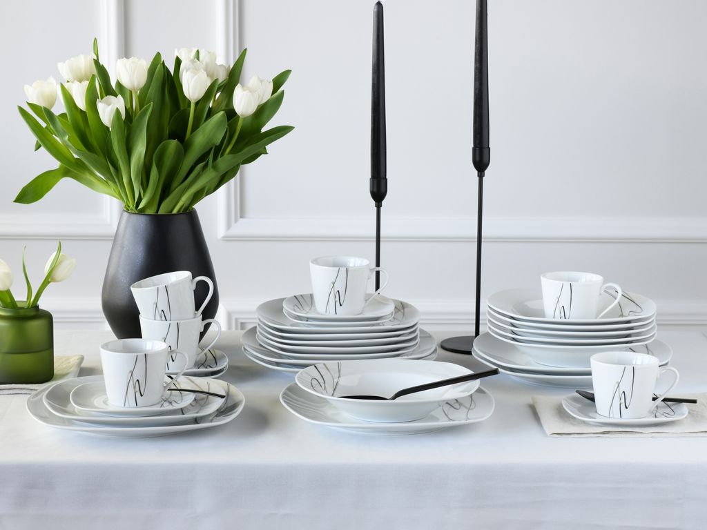 A table setting with white tulips, black candles, and a dinnerware set.