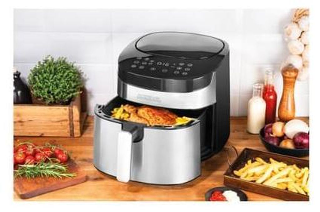 An air fryer with food inside and on a wooden countertop with ingredients.