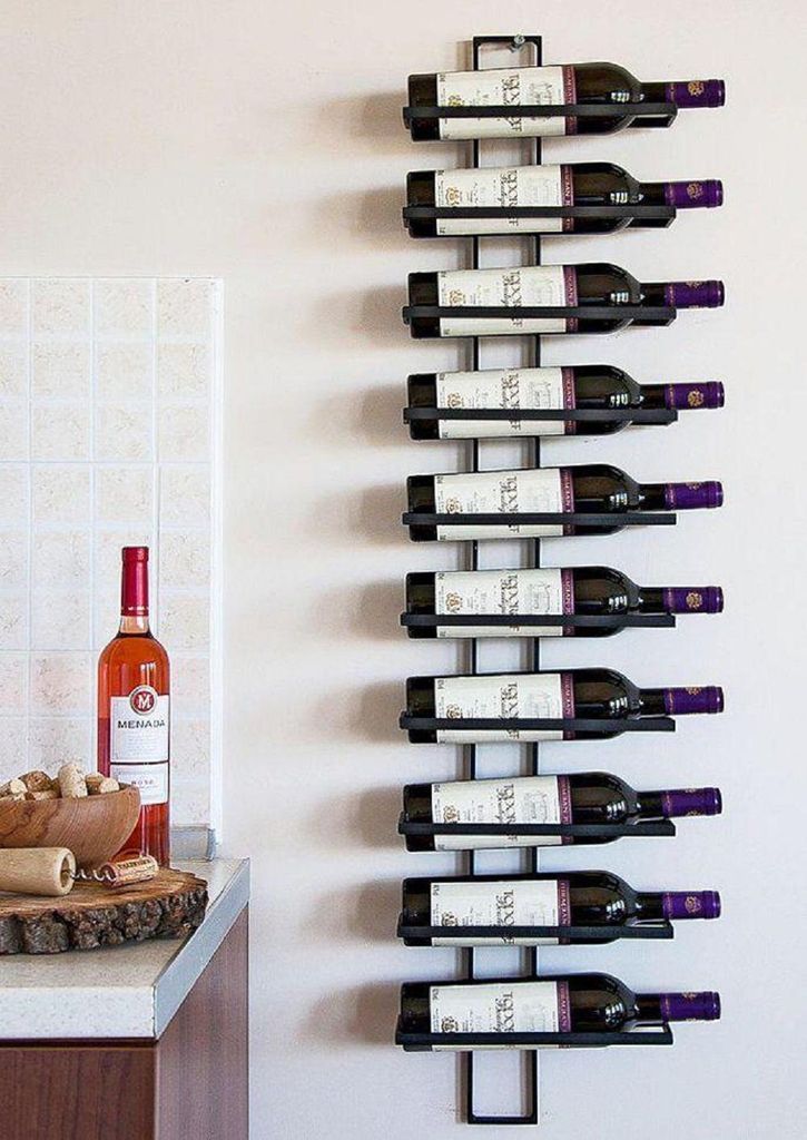 A black metal wine rack mounted on a white wall, holding ten bottles of wine. A bottle of rose wine and a bowl of corks are on a countertop to the left.