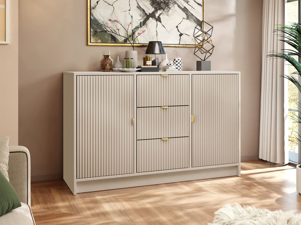 A sandbeige sideboard with fluted doors and drawers, decorated with a lamp, vases, and a sculpture, placed in a room with a painting on the wall and a plant in the background.