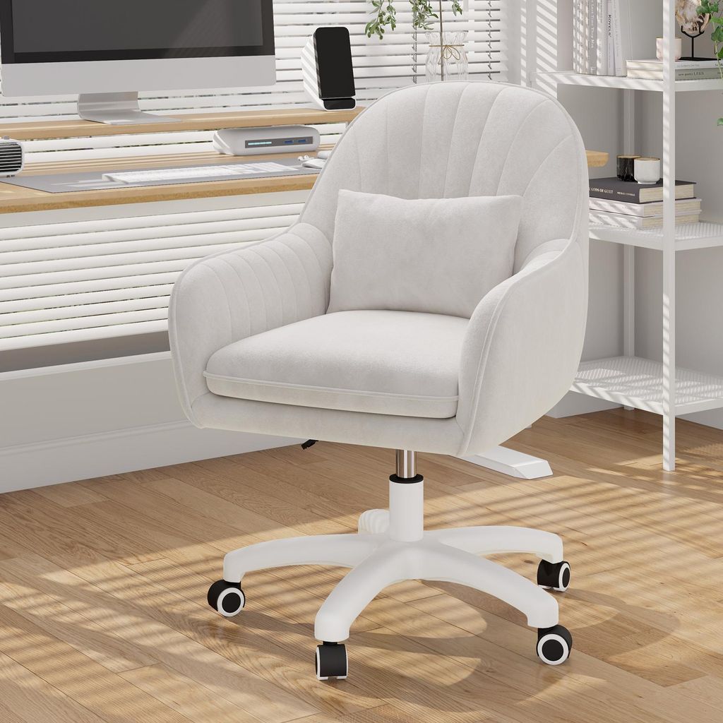 A white velvet office chair with a small pillow is shown in a well-lit room with wooden floors and blinds.