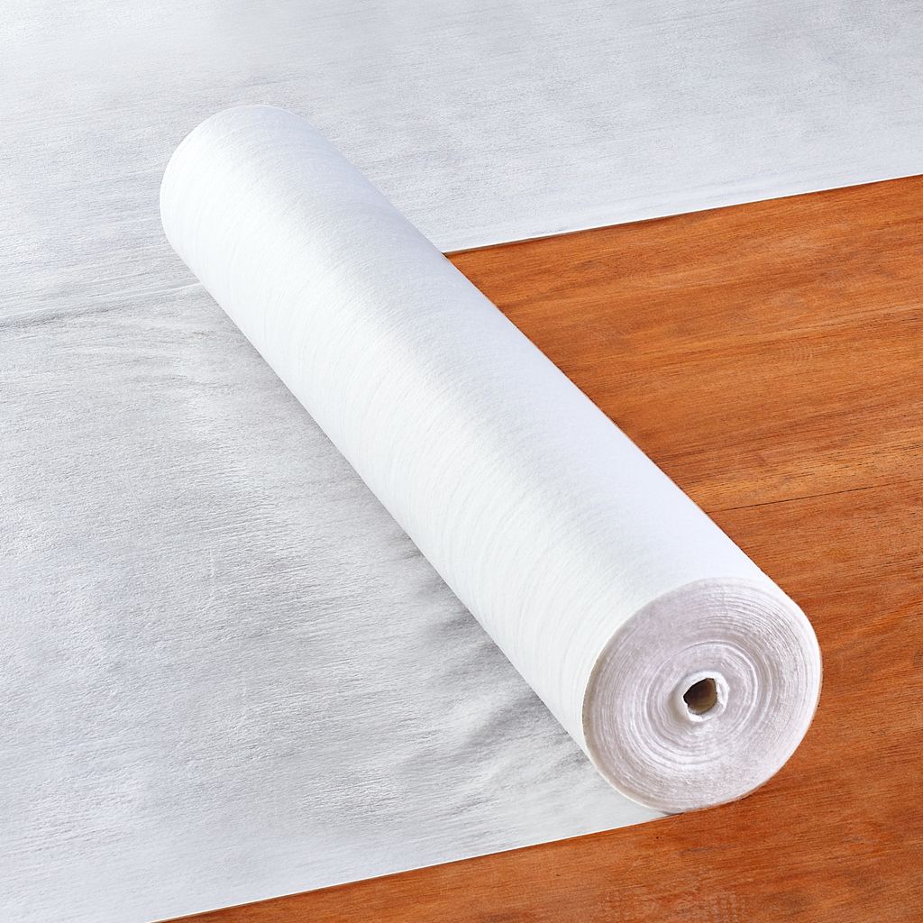 A roll of white fabric protection film is lying on a wooden floor.