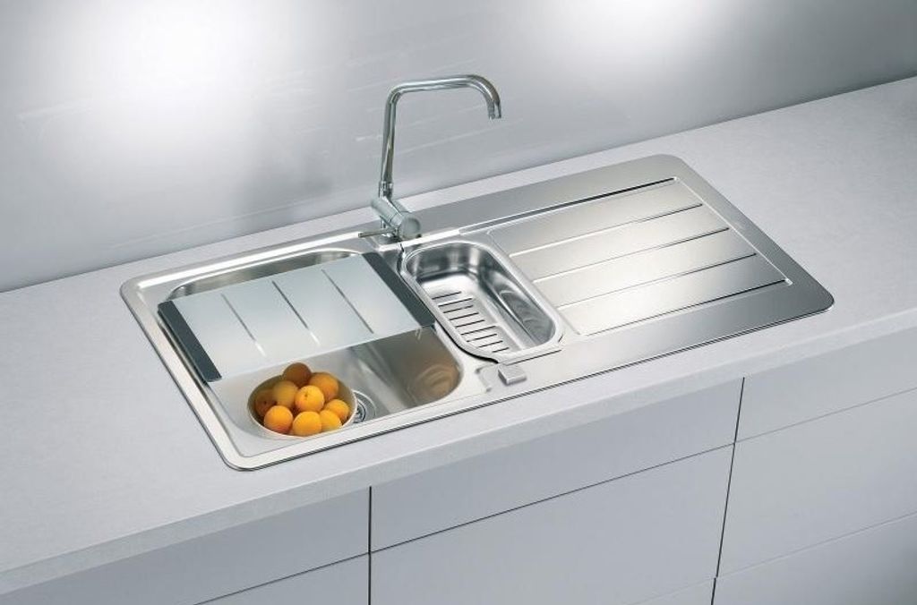 A stainless steel kitchen sink with a faucet, a cutting board, a drainer basket, and a bowl of oranges.