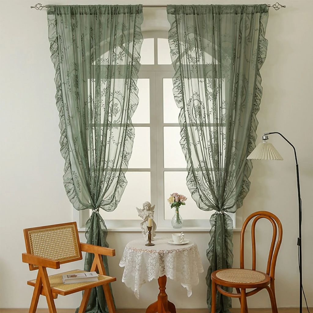 A room interior with a window dressed with green lace curtains, a small round table with a figurine and a teacup, and two chairs.