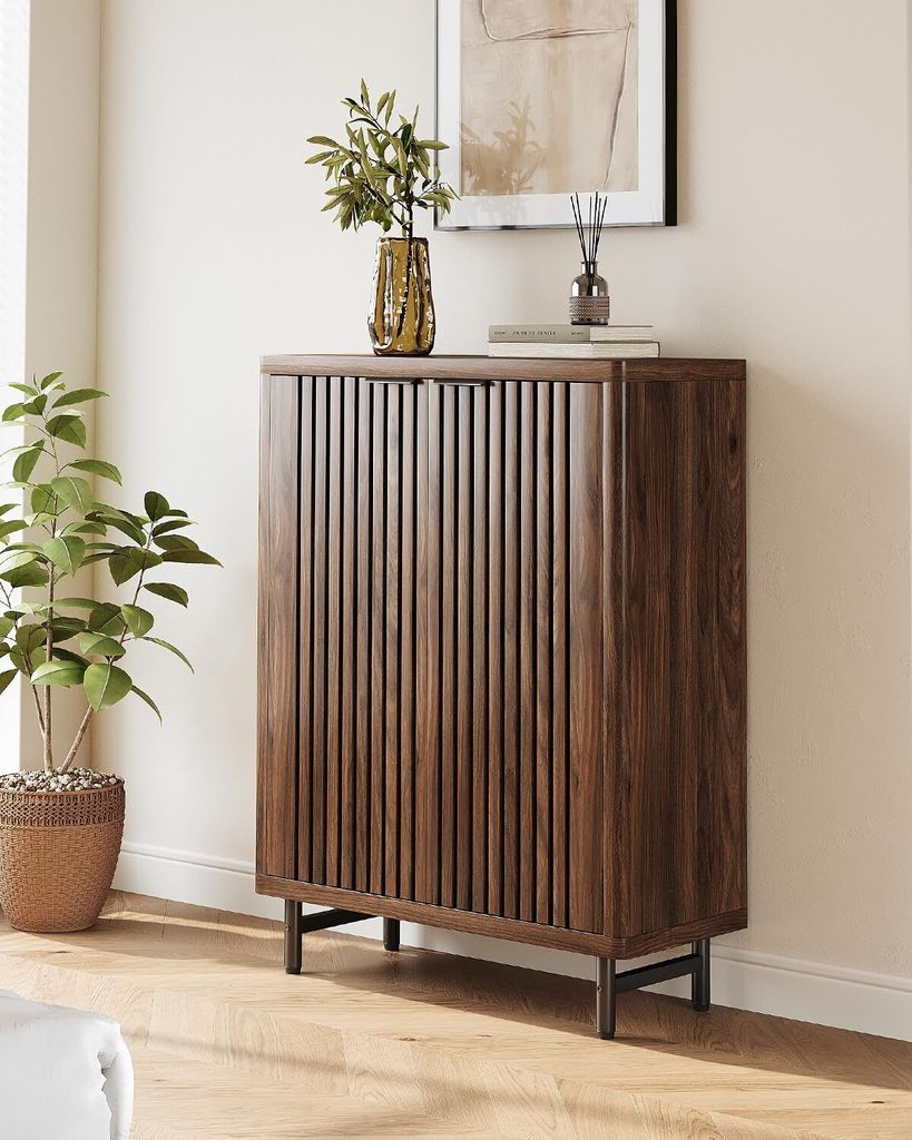 A dark wood cabinet with slatted doors stands in a room with a plant and artwork.