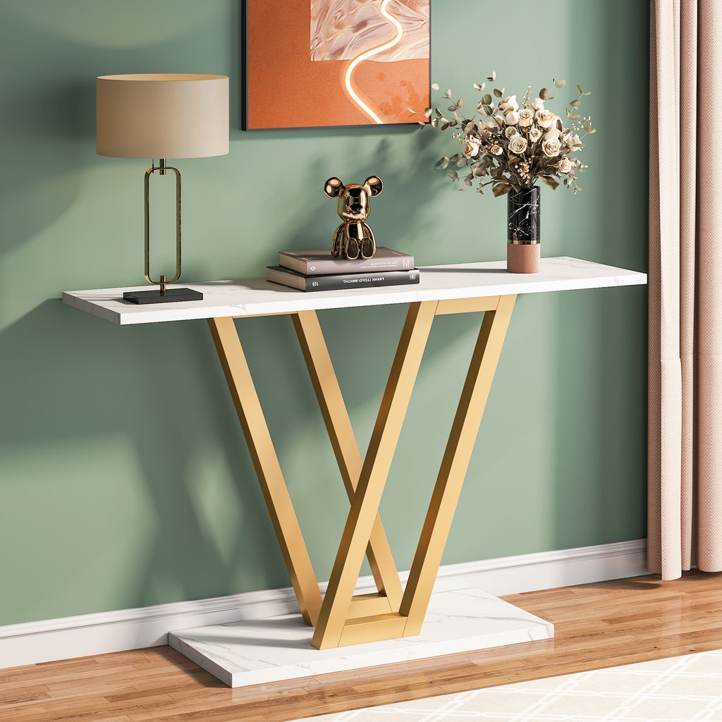 A console table with a lamp, books, and a vase of flowers on it, placed against a green wall.