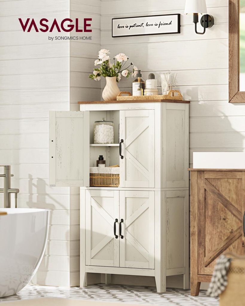 A white wooden bathroom cabinet with two doors at the bottom and a glass door at the top, filled with bathroom essentials and decorative items. A bathtub is visible to the left, and a wooden vanity to the right.