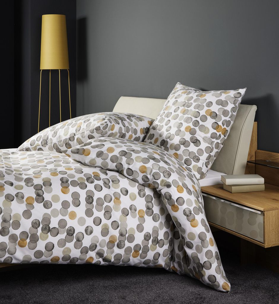 A neatly made bed with a polka dot duvet cover and pillows, next to a bedside table and a floor lamp.