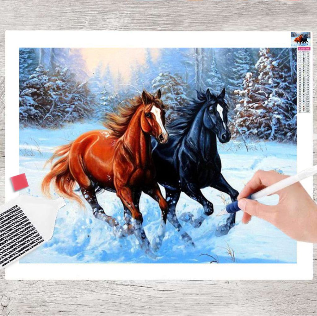 A diamond painting kit with two horses running in the snow, with a hand holding a tool to place diamonds.