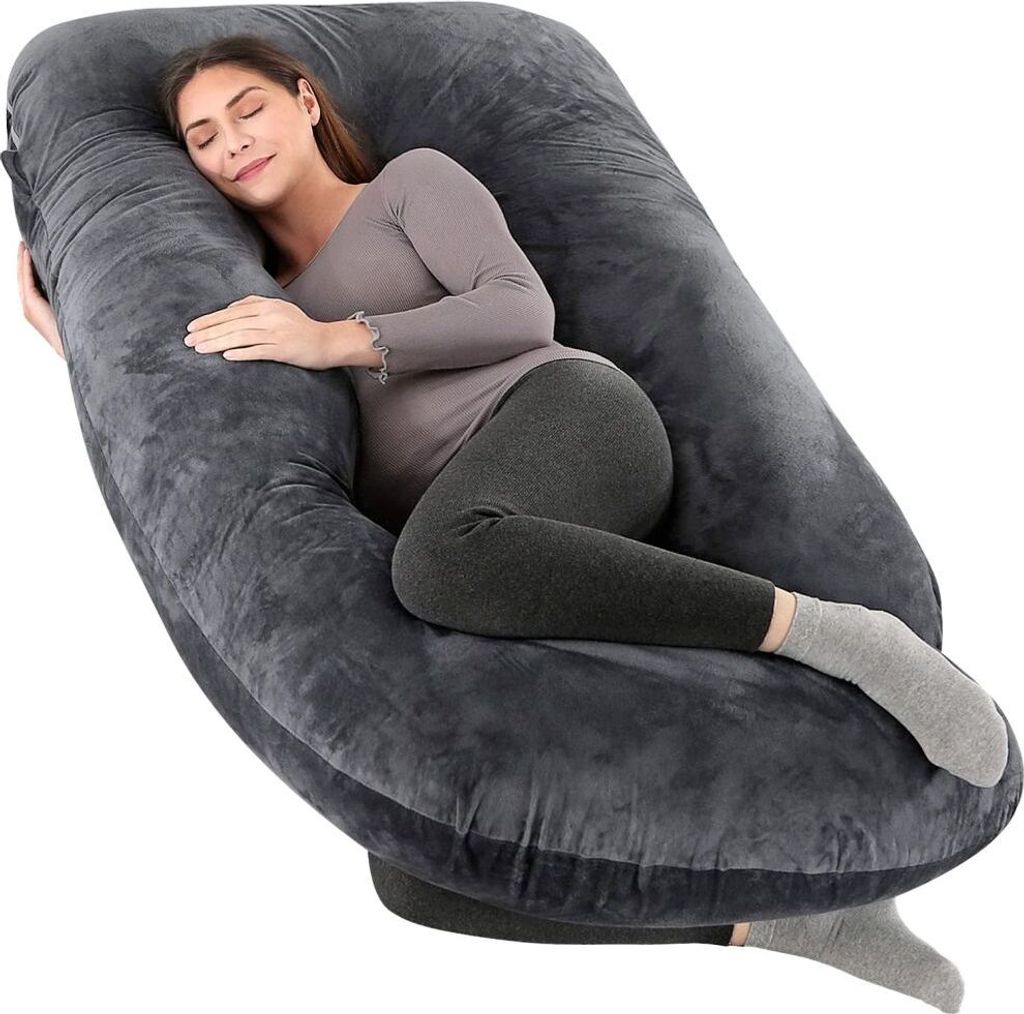 A pregnant woman is sleeping comfortably on a large, U-shaped pillow.