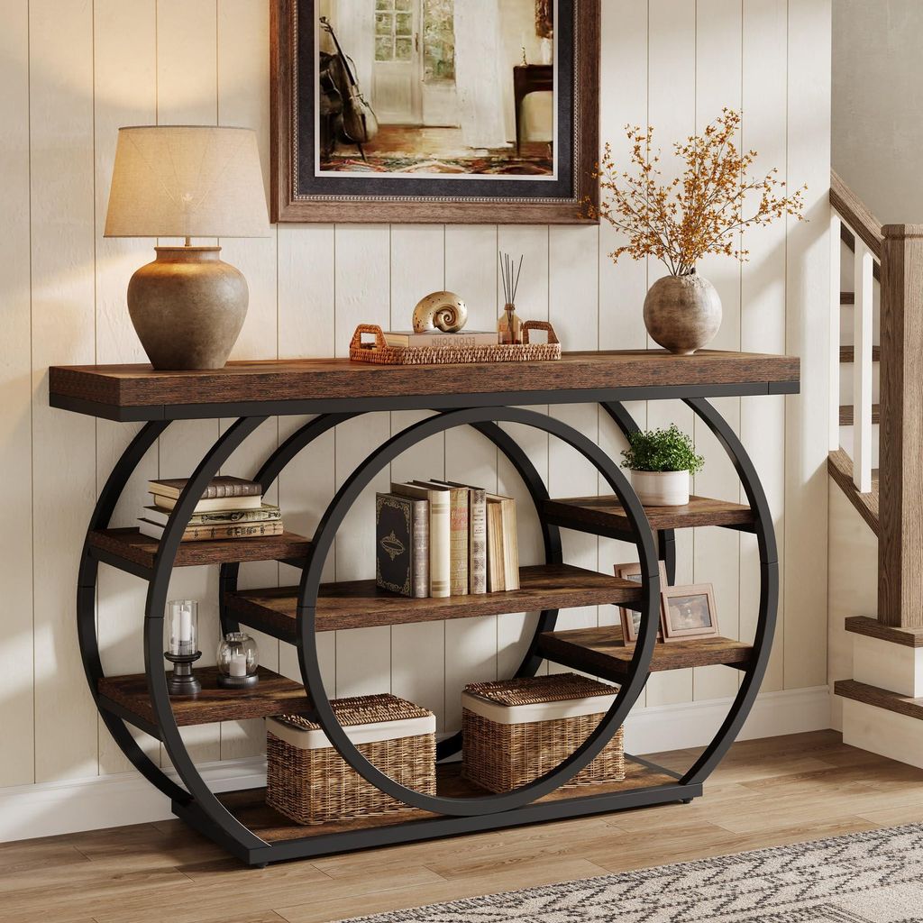 A console table with shelves is decorated with books, a lamp, and decorative items, placed in a hallway next to a staircase.