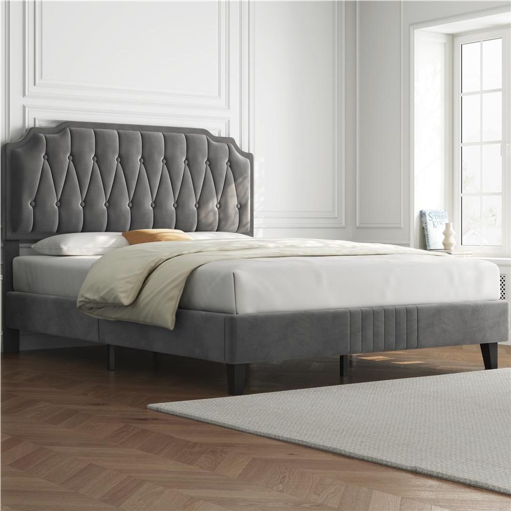 A dark gray upholstered bed with a tufted headboard is shown in a well-lit room with white walls and a large window.