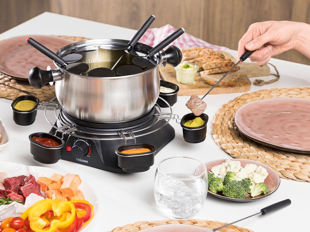 A family fondue set is being used at a table with various food items and dipping sauces.