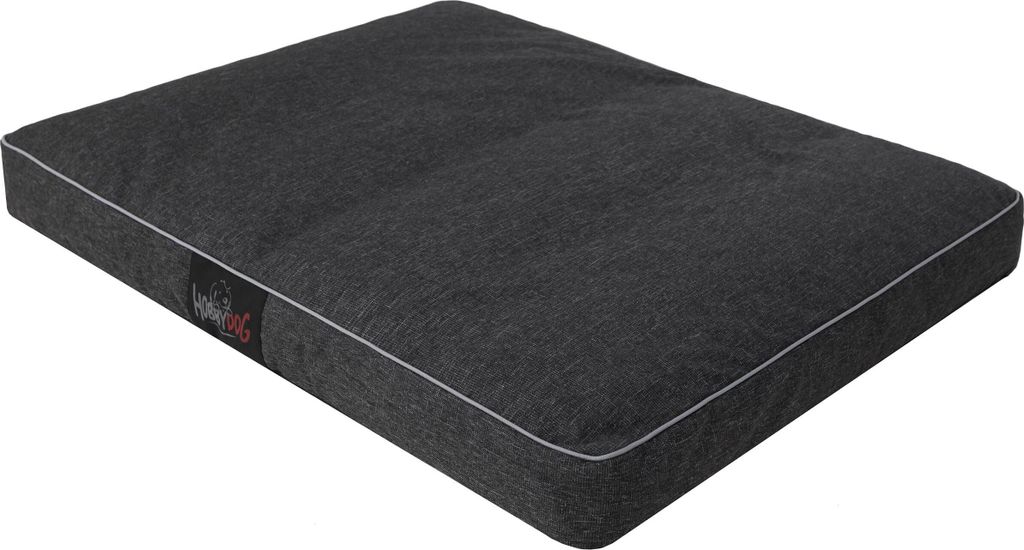 A dark gray dog bed with white piping, shown from a slightly elevated angle on a white background. A small black label with red and white text is visible on the left side of the bed.