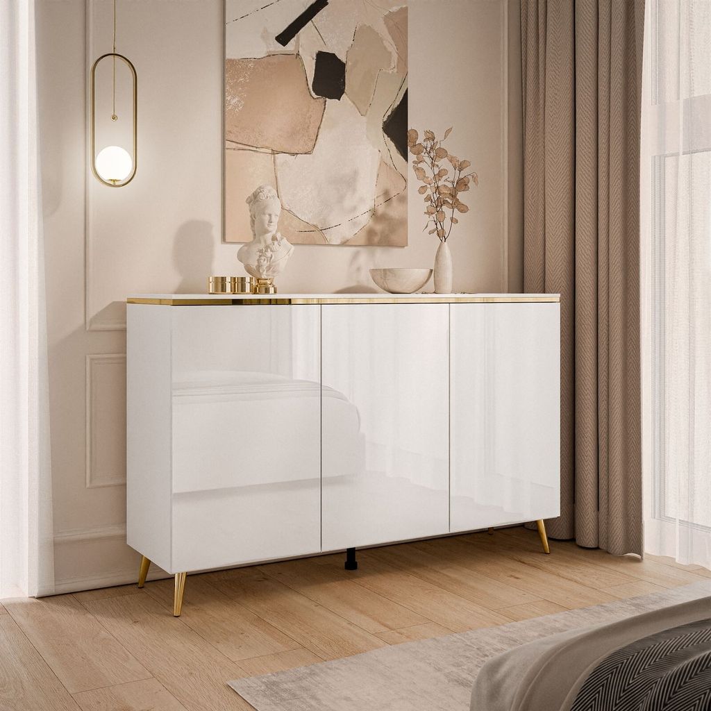 A white, high-gloss sideboard with gold legs and trim, displayed in a well-lit room with neutral-toned curtains and abstract art on the wall.