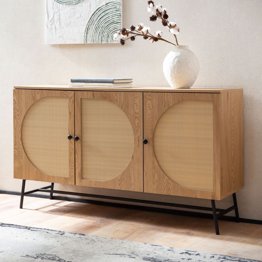 A wooden sideboard with rattan woven doors sits against a wall with artwork above it.