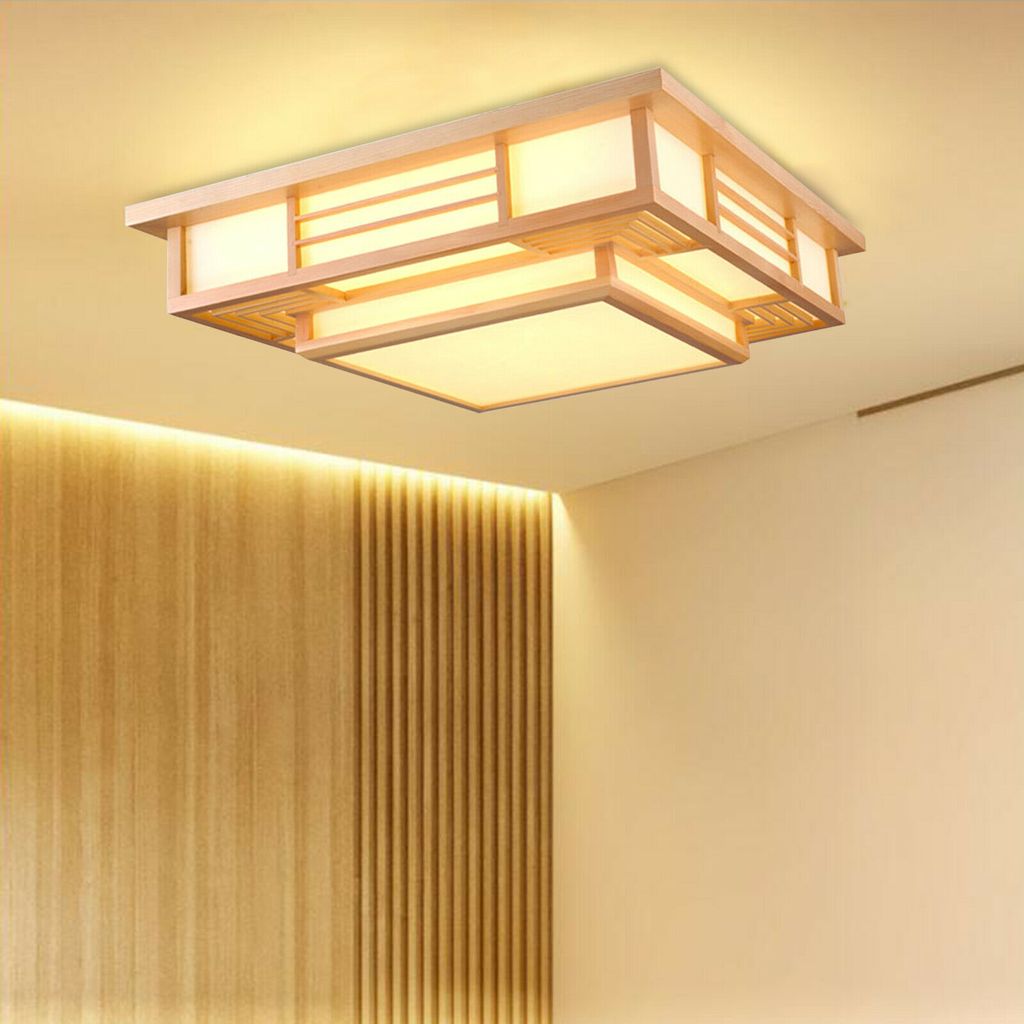 A modern wooden ceiling light fixture with a Japanese design, illuminated against a plain ceiling and a wood-paneled wall.