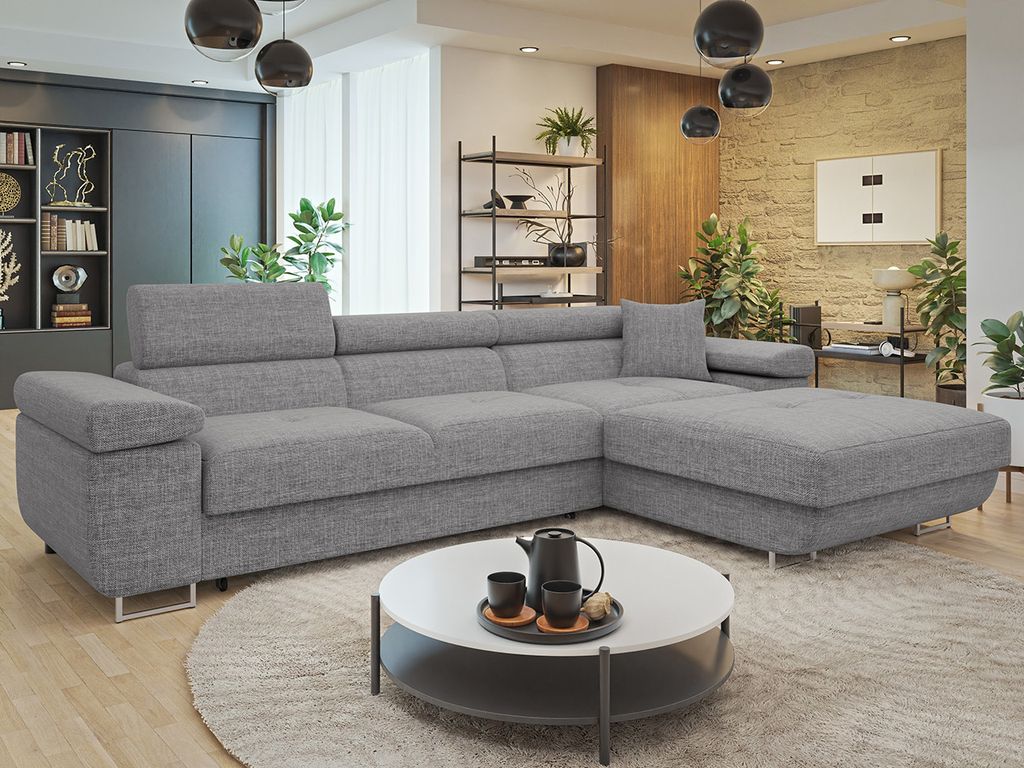 A modern living room with a gray sectional sofa, a round coffee table with a teapot and cups, and decorative shelves with plants and books.
