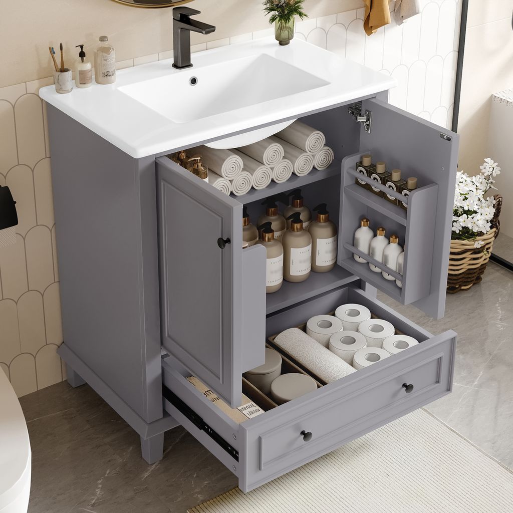 A grey bathroom vanity with a white ceramic sink, open doors revealing storage, and a partially open drawer filled with toiletries.