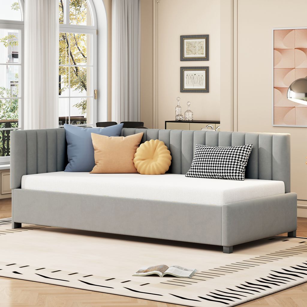 A daybed with several decorative pillows is shown in a well-lit room with large windows and a rug.