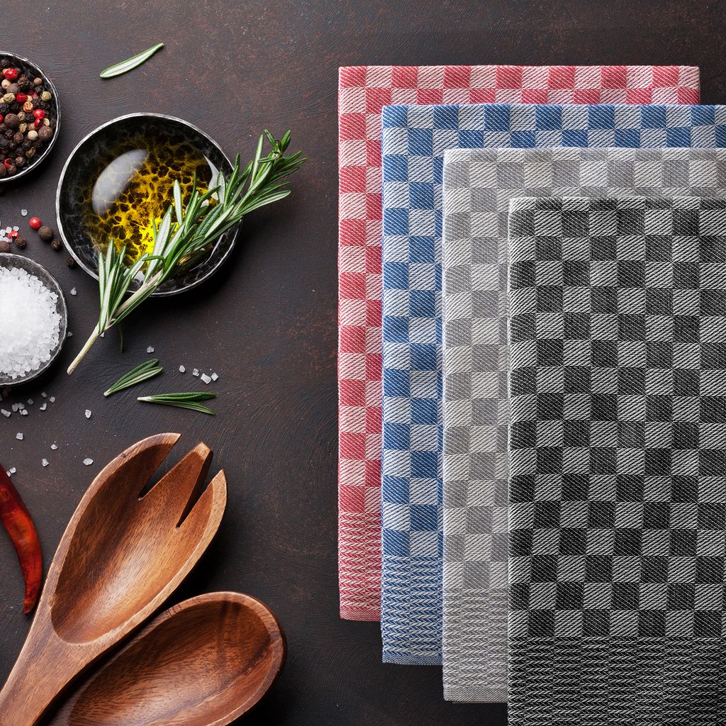 A collection of checkered kitchen towels arranged neatly, with cooking ingredients like olive oil, rosemary, peppercorns, and salt in bowls, along with wooden serving utensils, laid out on a dark brown surface.