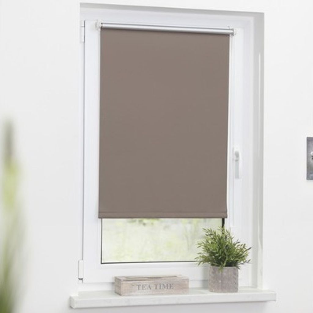 A taupe roller blind is shown covering most of a window, with a small plant and a wooden box on the windowsill below.