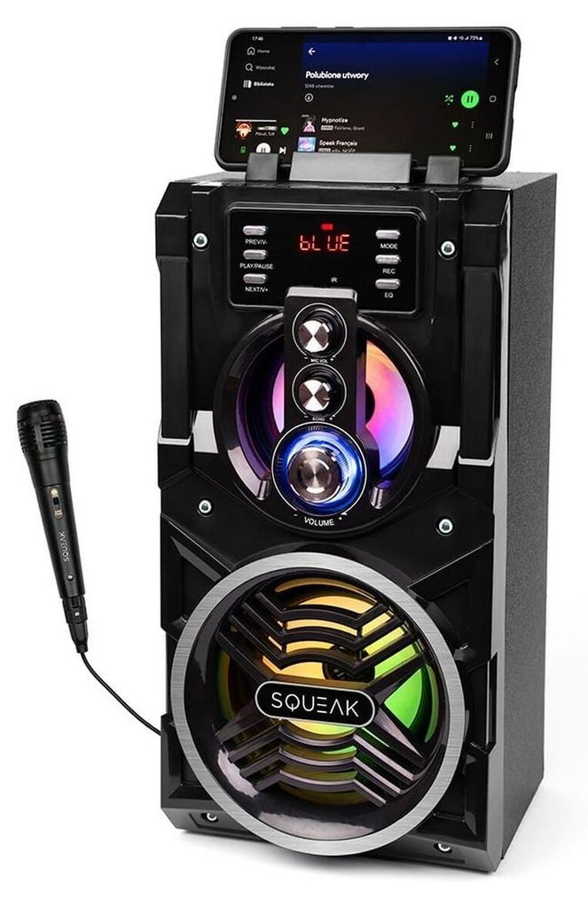 A black portable Bluetooth speaker with a smartphone docked on top, displaying a music app. A microphone is connected to the side.