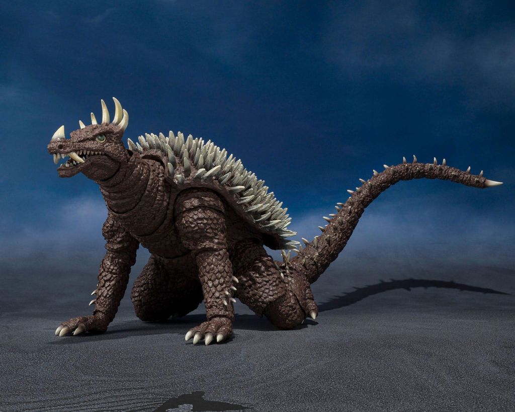 A Godzilla-like monster figure on a dark, textured surface with a dark blue background.