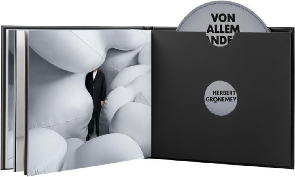 An open book-style case with a CD and a book inside. The book has a person in a suit standing among white inflatable shapes.
