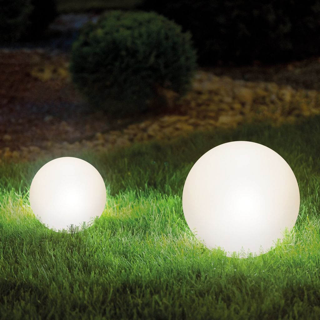 Two illuminated spherical garden lights on a lawn at night.