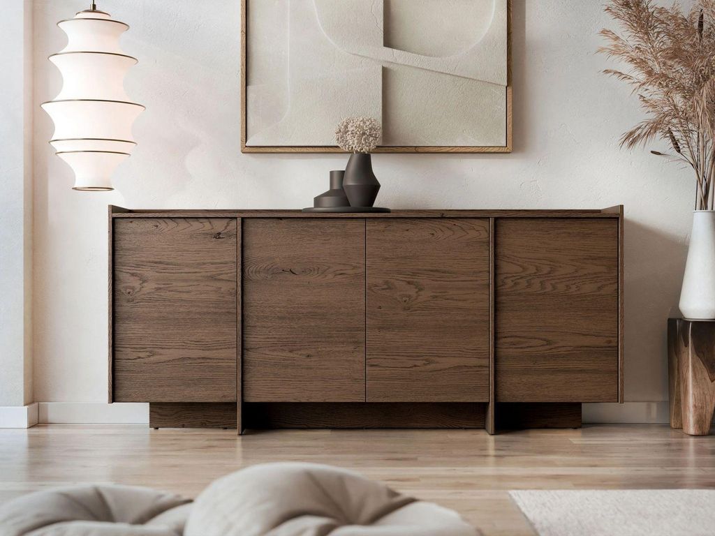 A wooden sideboard with four doors is displayed in a well-lit, modern living room setting, adorned with decorative vases and dried flowers.