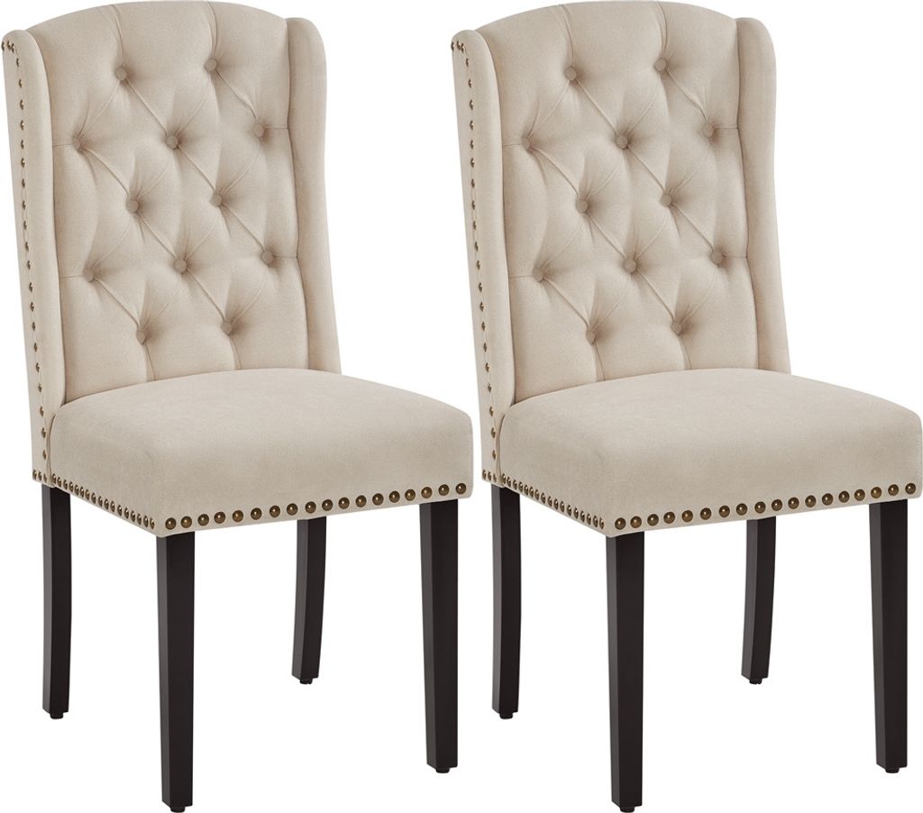 Two beige upholstered dining chairs with dark wood legs and nailhead trim are shown against a white background.