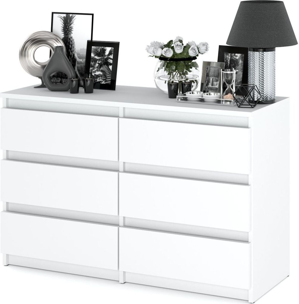 A white dresser with decorative items on top, including framed pictures, a vase of flowers, and a lamp.