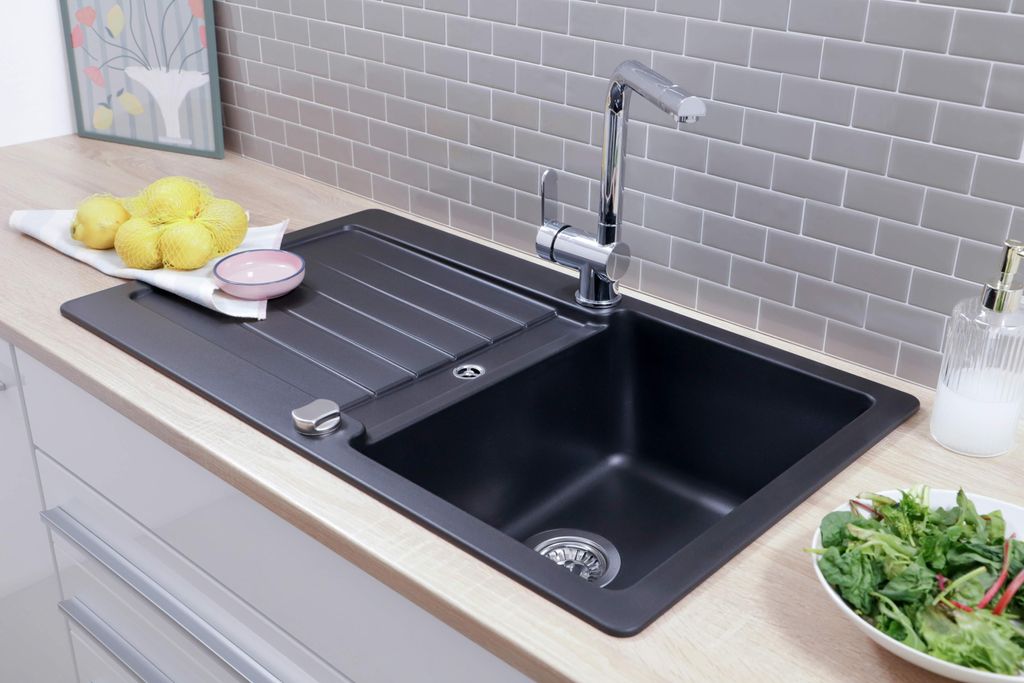 A black kitchen sink with a faucet, lemons, and a bowl of salad on a wooden countertop.