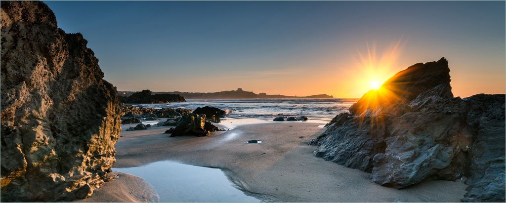 Wallario selbstklebendes Poster - Sonnenuntergang hinter einem Felsen am Strand, Größe: 80 x 200 cm