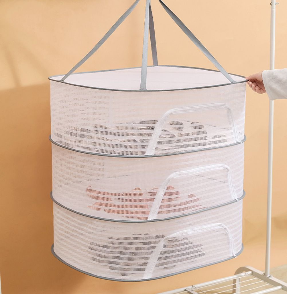 A three-tiered mesh drying rack hanging against a light orange wall, with a white clothing rack visible on the right.