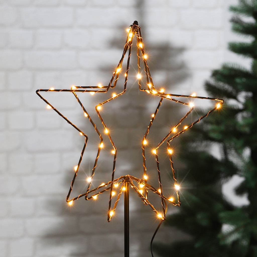 A lighted star decoration is shown in front of a brick wall and a Christmas tree.