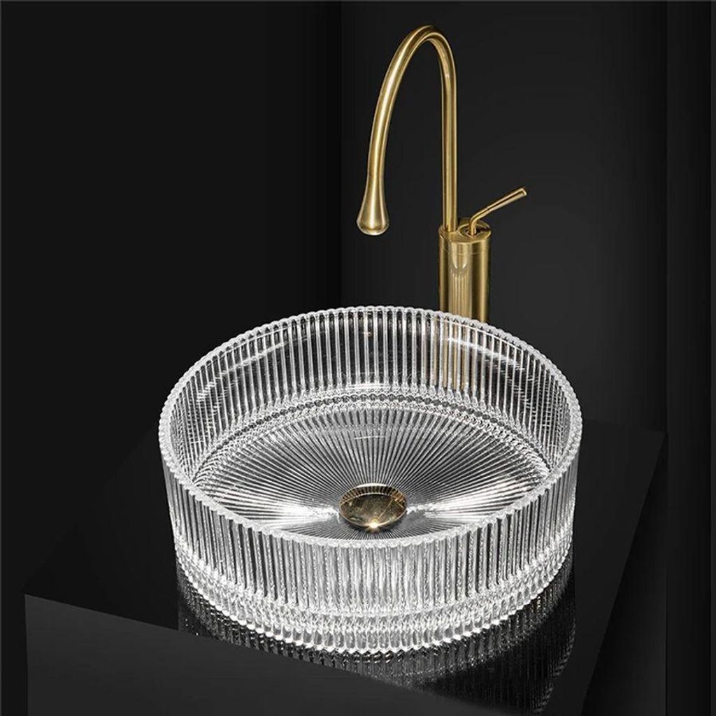 A clear glass basin with a gold faucet against a black background.