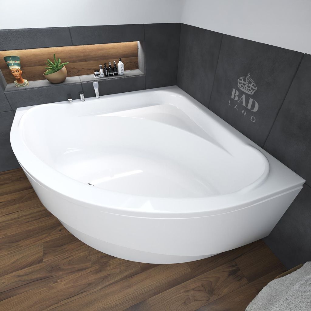 A white corner bathtub is shown in a modern bathroom with dark gray tiled walls and a wooden floor. A recessed shelf above the tub holds decorative items and toiletries.